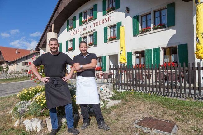 Deux hommes en tablier se tiennent devant un bâtiment.