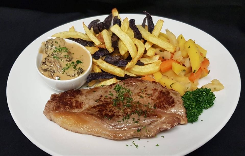 Une assiette blanche garnie d'un steak, de frites et de légumes.