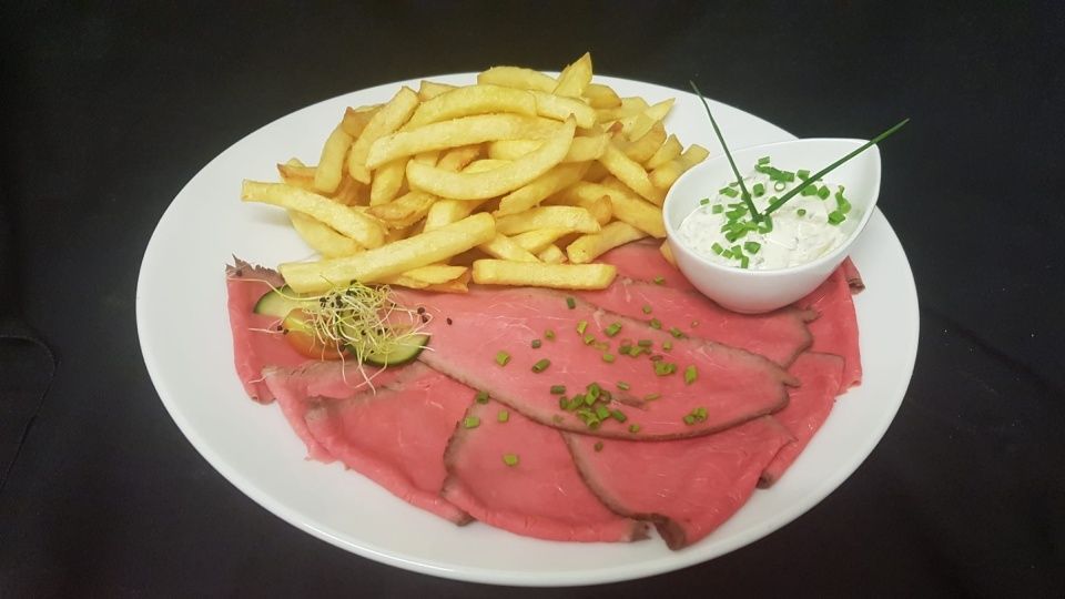 Une assiette blanche garnie de viande et de frites sur une table noire.