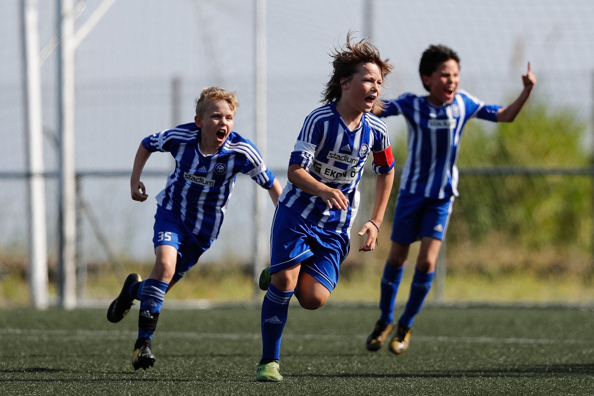 Jugadores de fútbol con uniformes azules y blancos celebrando un gol en un campo verde.
