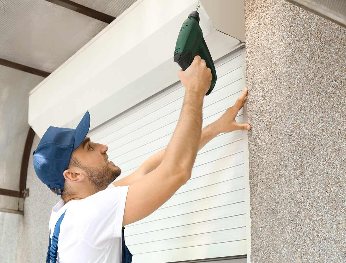 Un hombre está instalando una persiana enrollable en un edificio.