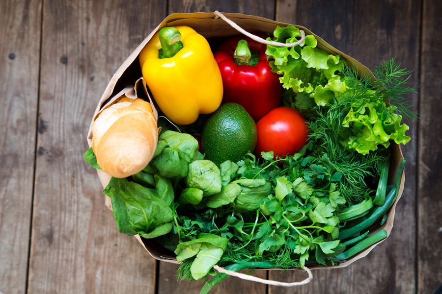 Panier de légumes frais sur une table en bois, comprenant poivrons, laitue, herbes aromatiques, tomates, oignon et avocat.
