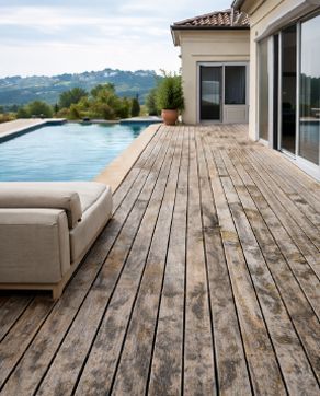 Terraza de madera con piscina, casa beige y sofá con vistas a las ondulantes colinas verdes.