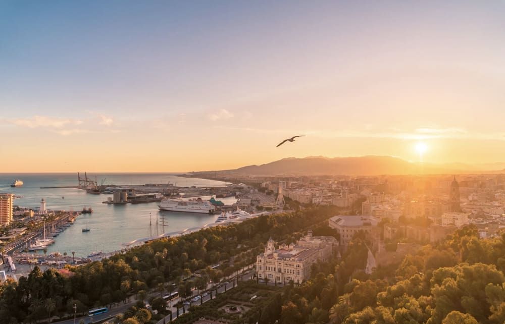 Atardecer en Málaga, España; vista del puerto, los edificios de la ciudad y el océano. Cálida luz dorada.