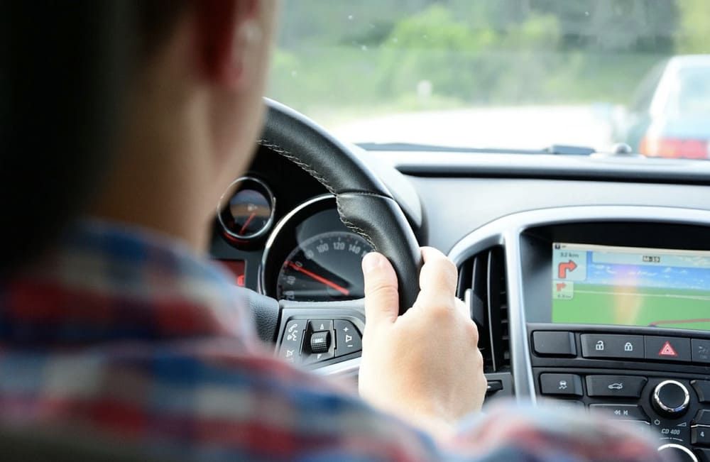 Persona conduciendo un automóvil, manos en el volante, pantalla de navegación GPS visible.