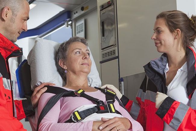 Des ambulanciers aident un patient souriant, allongé sur une civière à l'intérieur d'une ambulance.