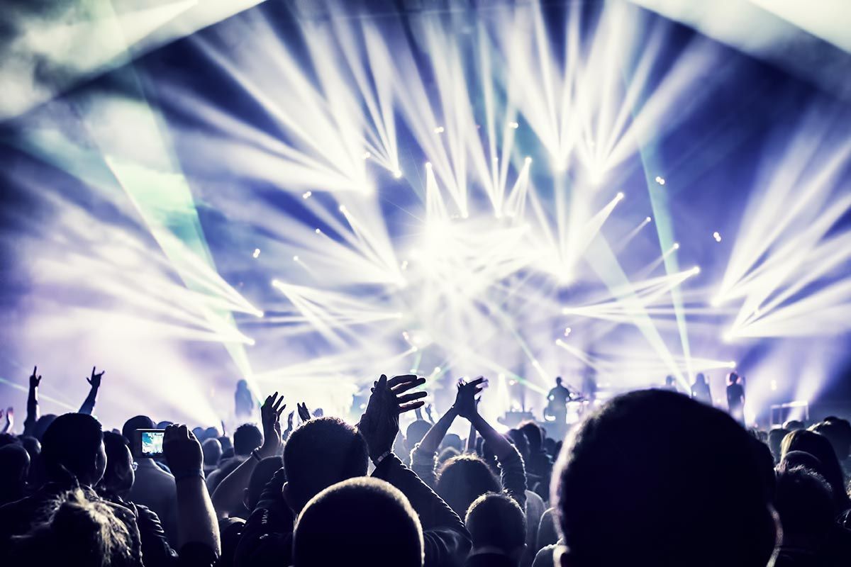 La foule du concert se détachant en silhouette sur les lumières et les faisceaux blancs éclatants de la scène.