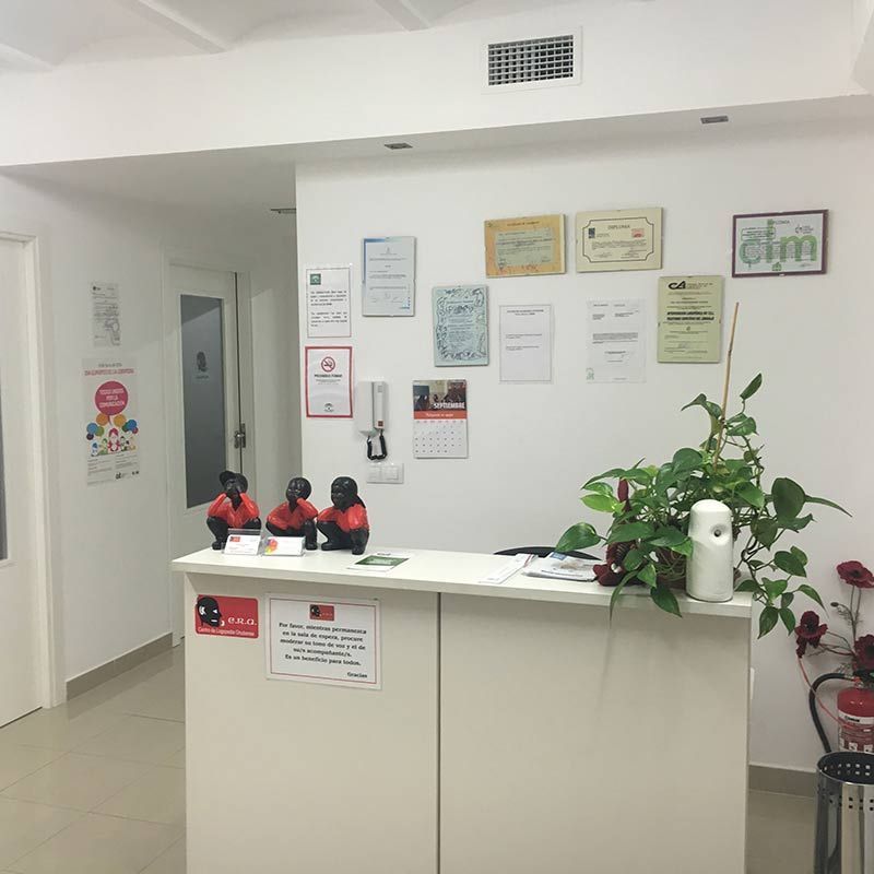 Un pequeño mostrador de recepción blanco en el vestíbulo de una clínica, con certificados en la pared y una planta en maceta cerca.