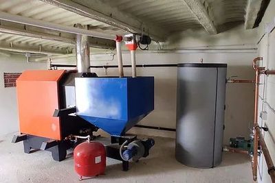 Unidades de calefacción industrial con depósitos naranjas y azules en una sala de calderas en el sótano.