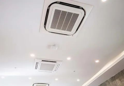 Techo con rejillas de ventilación cuadradas y luces empotradas en una habitación blanca.