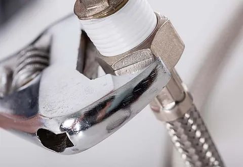 Primer plano de una llave inglesa apretando un conector de manguera cromado en un tubo roscado blanco.