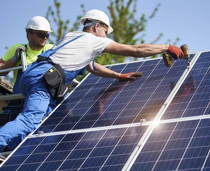 Trabajadores limpiando paneles solares en un tejado con cascos y equipo de seguridad.