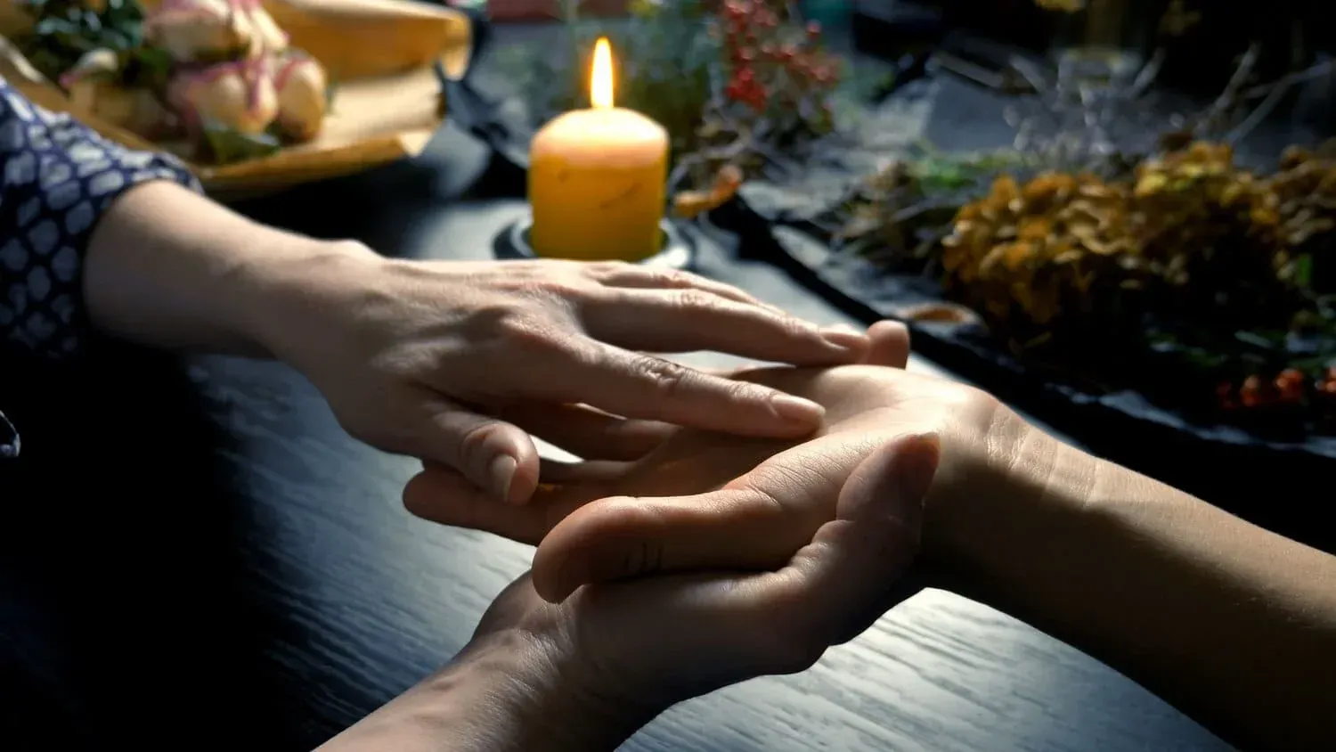 Manos leídas por otra mano, vela y decoraciones sobre una mesa oscura.