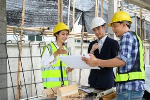 Eine Gruppe Bauarbeiter schaut sich auf einer Baustelle einen Bauplan an. Hackovic e.K.