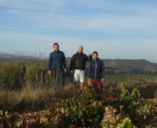 Tres hombres están parados en un campo con una montaña al fondo.
