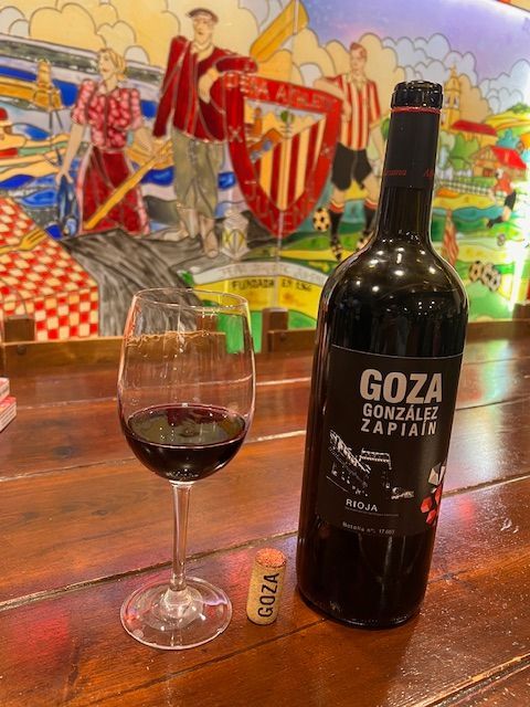 Una botella de vino goza y una copa de vino en una mesa de madera.