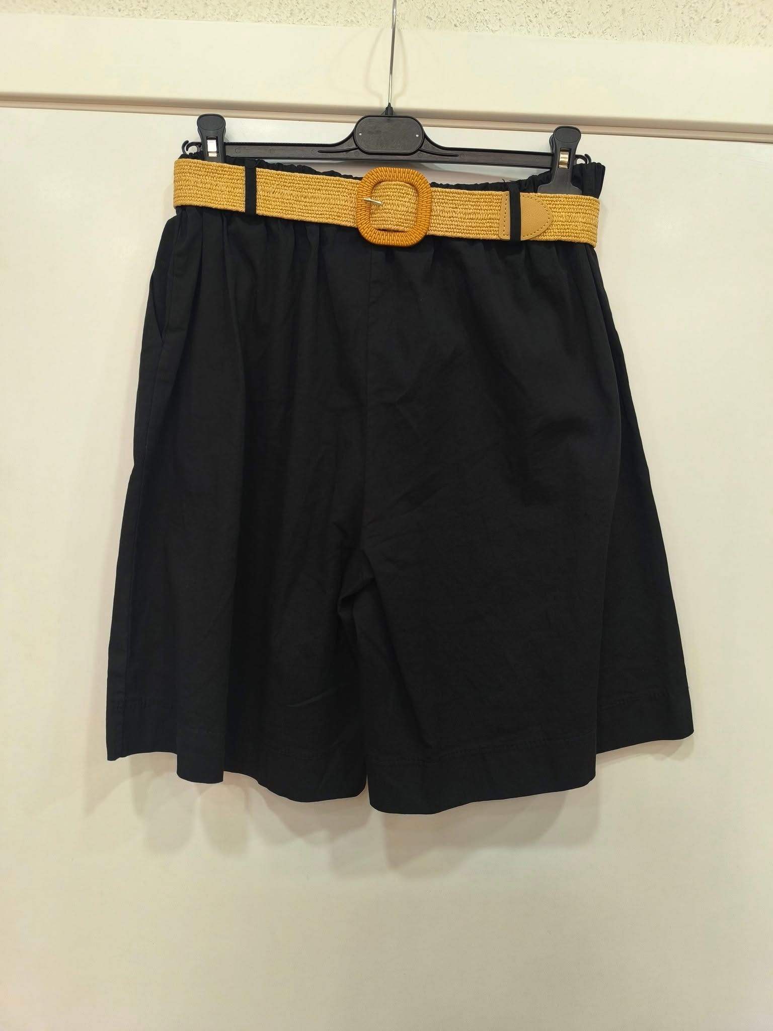 Un par de pantalones cortos negros con un cinturón dorado colgando de una percha.