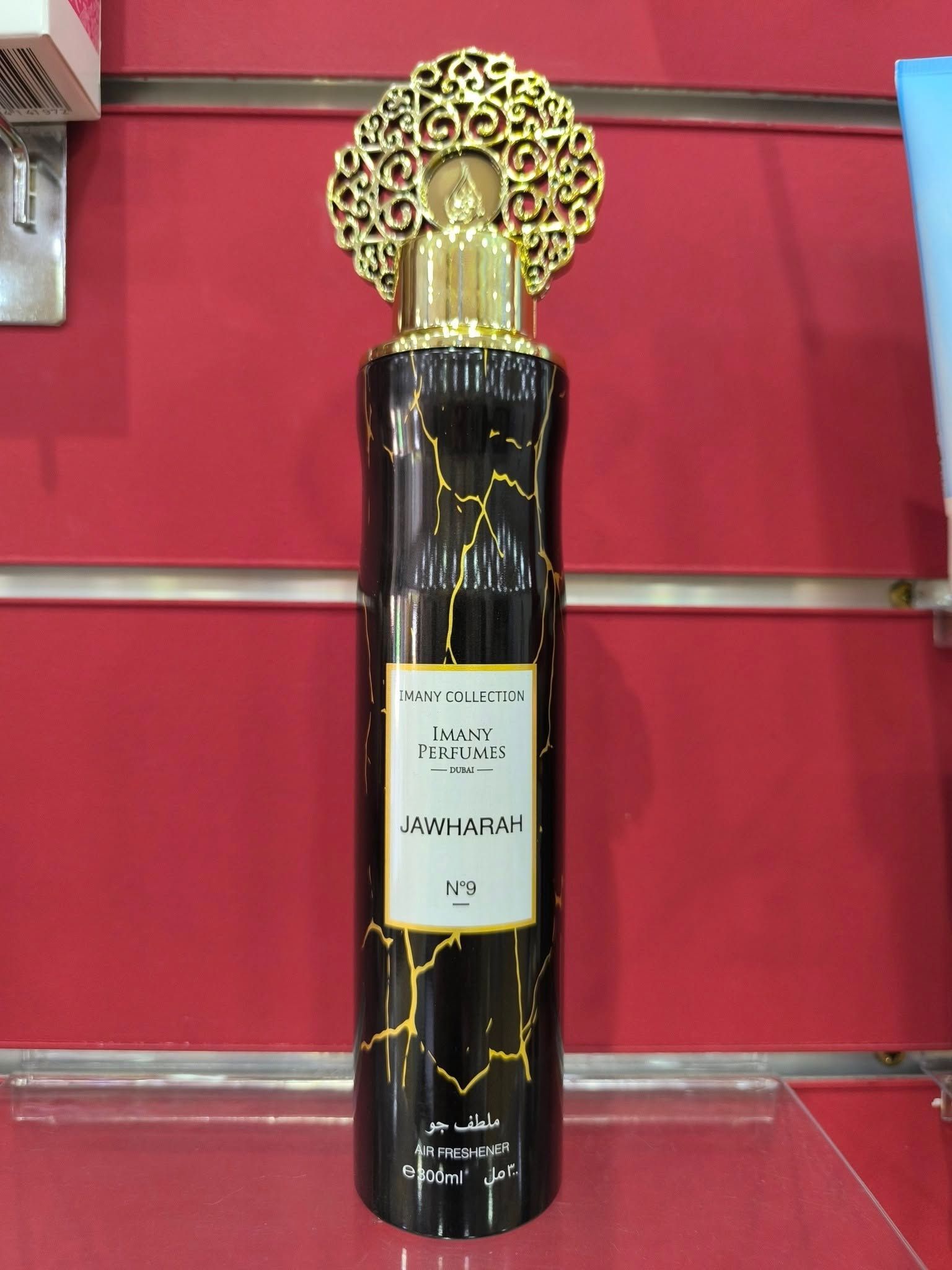 Un frasco de perfume está sobre un estante frente a una pared roja.