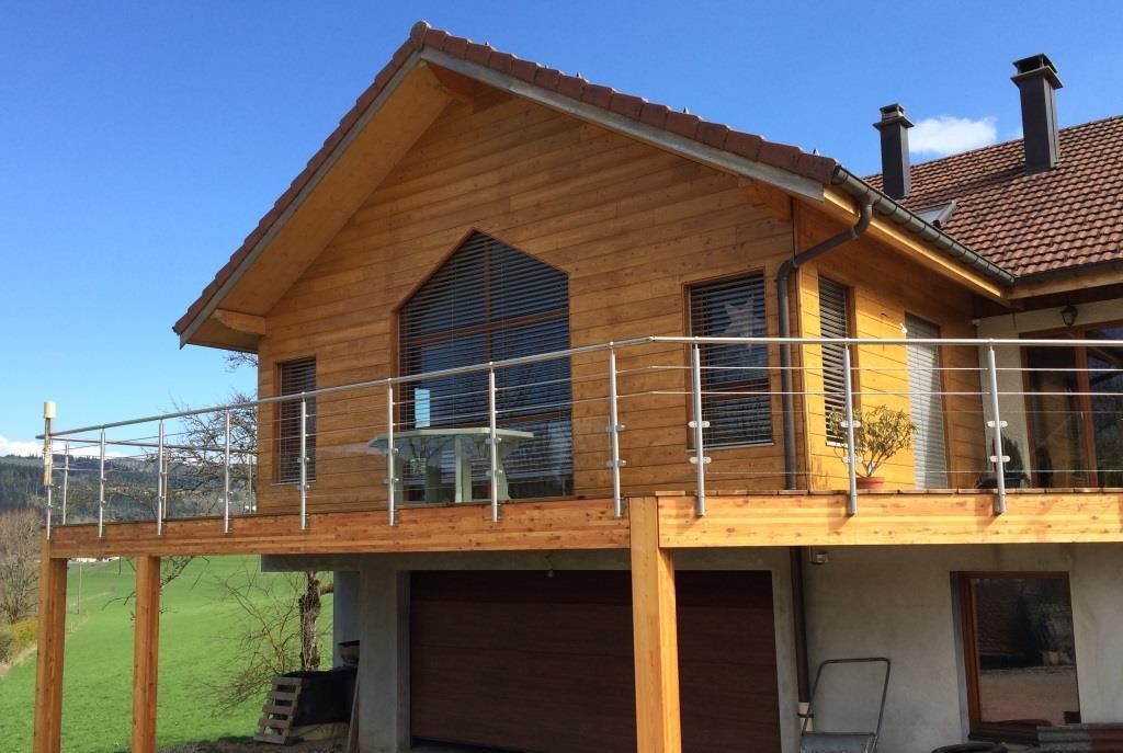 Partie surélevée d'une maison en bois avec garde-corps en inox et verre.