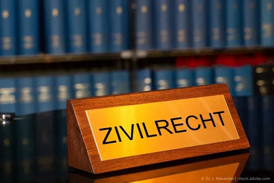 Ein Schreibtischschild mit der Aufschrift „ZIVILRECHT“ vor Regalen voller blauer juristischer Bücher.