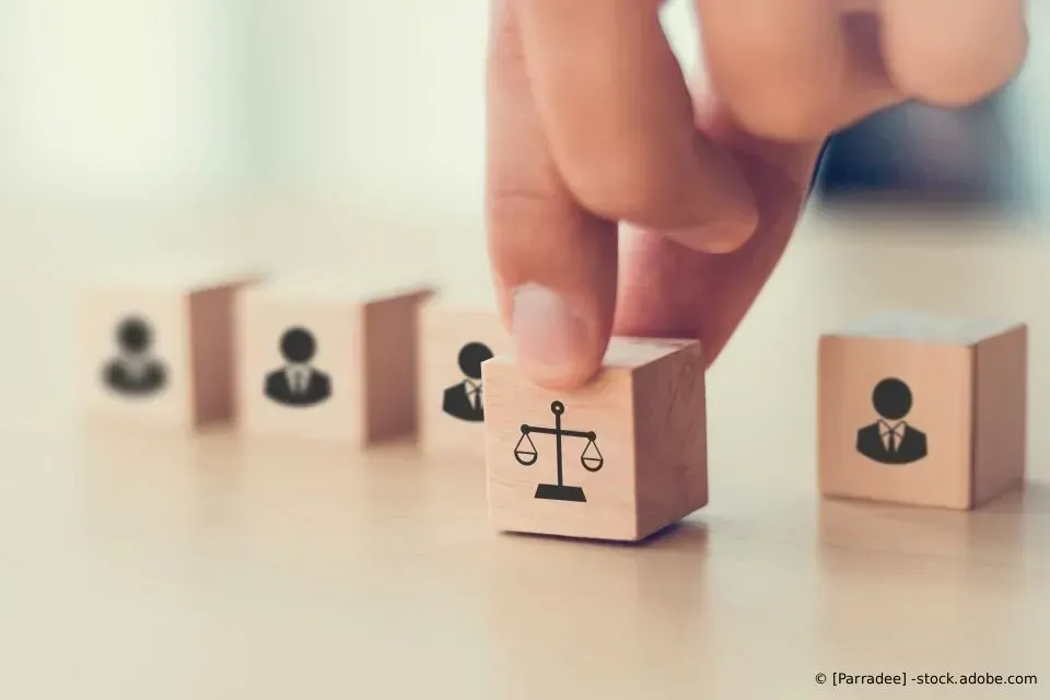 Eine Hand platziert einen Holzblock mit einem Symbol der Justitia zwischen anderen Blöcken mit Personensymbolen.