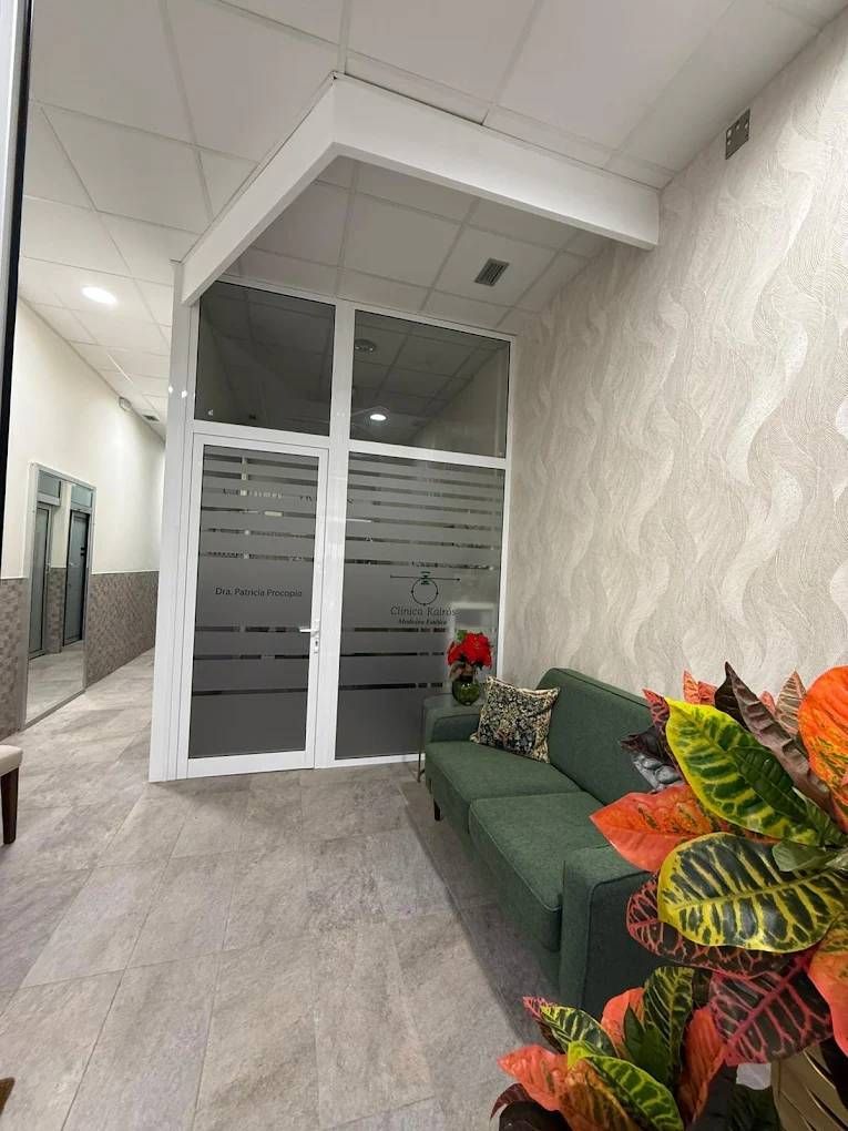 Una sala de espera con un sofá verde, una puerta de vidrio esmerilado y un papel tapiz estampado.