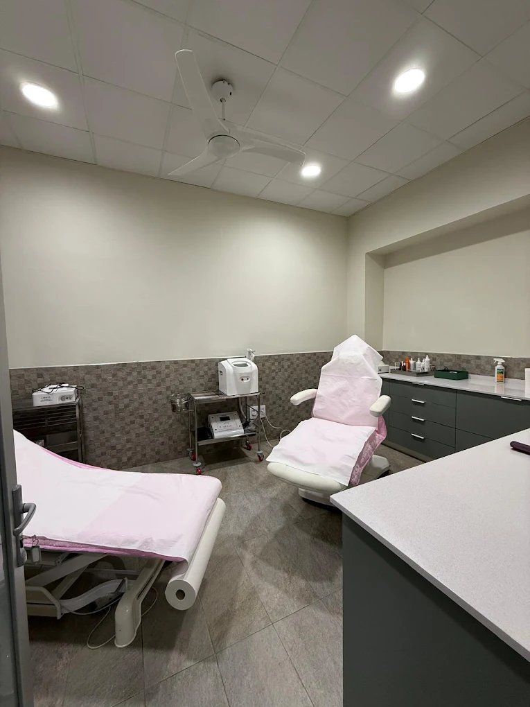 Sala de tratamiento médico con mesa de exploración, sillón reclinable tapizado en color rosa y equipamiento.