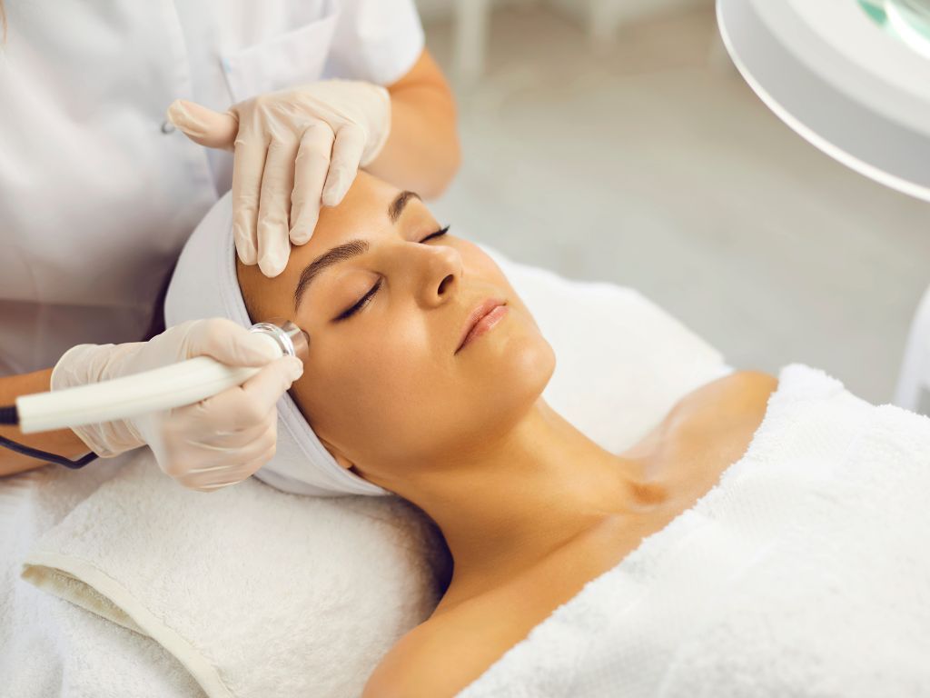 Mujer recibe un tratamiento facial en un spa, con los ojos cerrados, con un técnico utilizando un dispositivo.