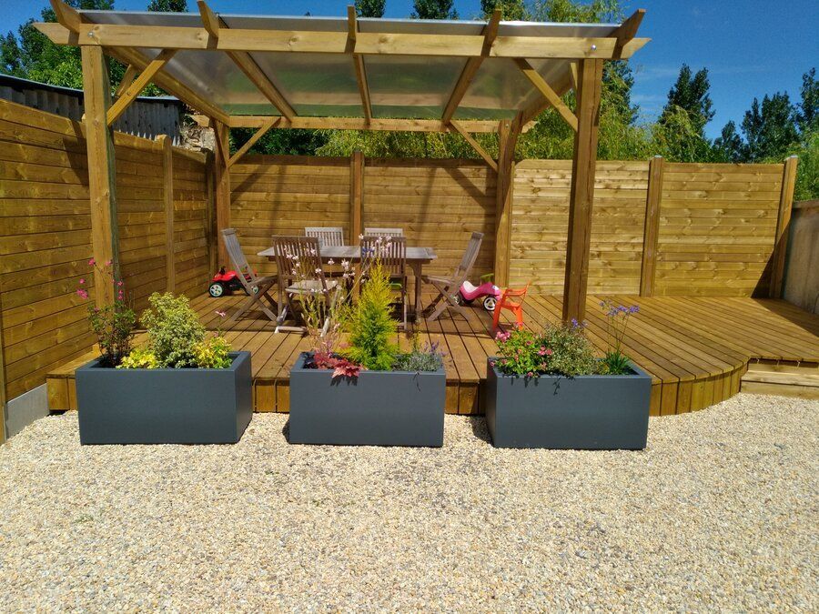 Terrasse en lattes de bois avec 3 jardinières noires devant