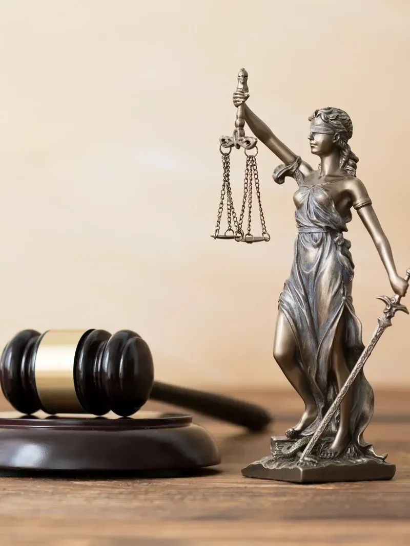 Eine Statue der Gerechtigkeit hält eine Waage und einen Hammer auf einem Holztisch.