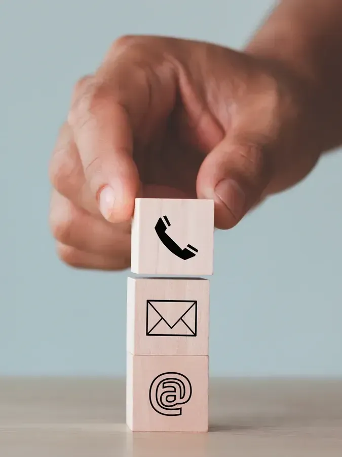 Eine Hand hält einen Stapel Holzklötze mit Kontaktsymbolen darauf.