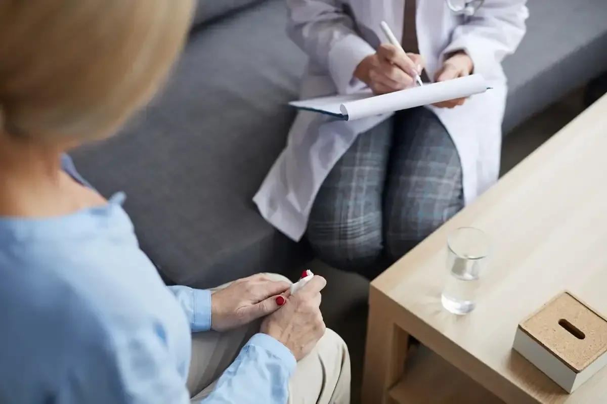 Una persona consulta con un médico en un consultorio. El médico toma notas.