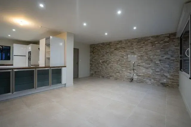 Pièce vide avec mur en pierre, coin cuisine et grande fenêtre.