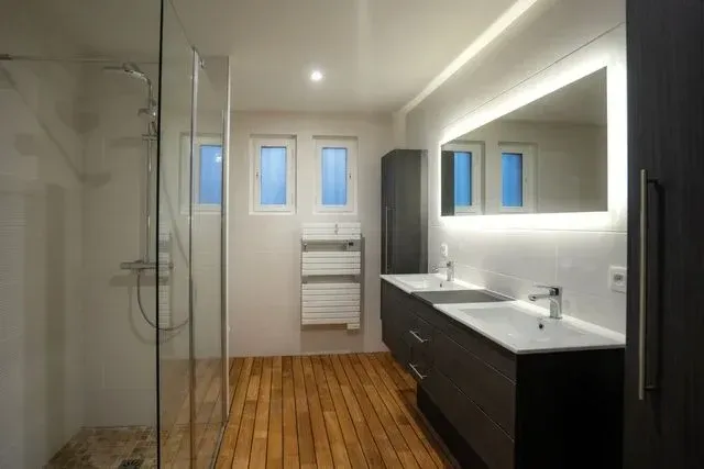 Salle de bain moderne avec douche en verre, double vasque et plancher en bois.