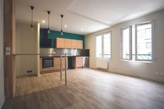 Appartement vide avec parquet, cuisine ouverte et mur d'accent bleu sarcelle.