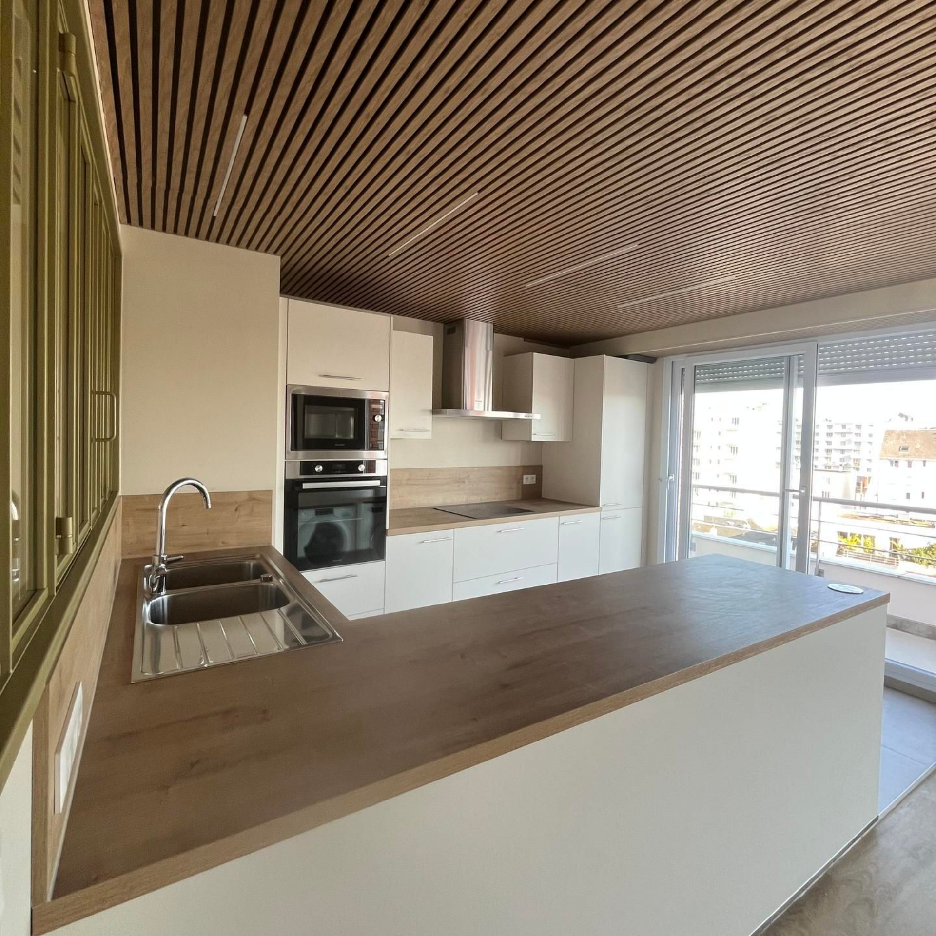 Cuisine moderne avec plafond en bois, armoires blanches et comptoir donnant sur un balcon.