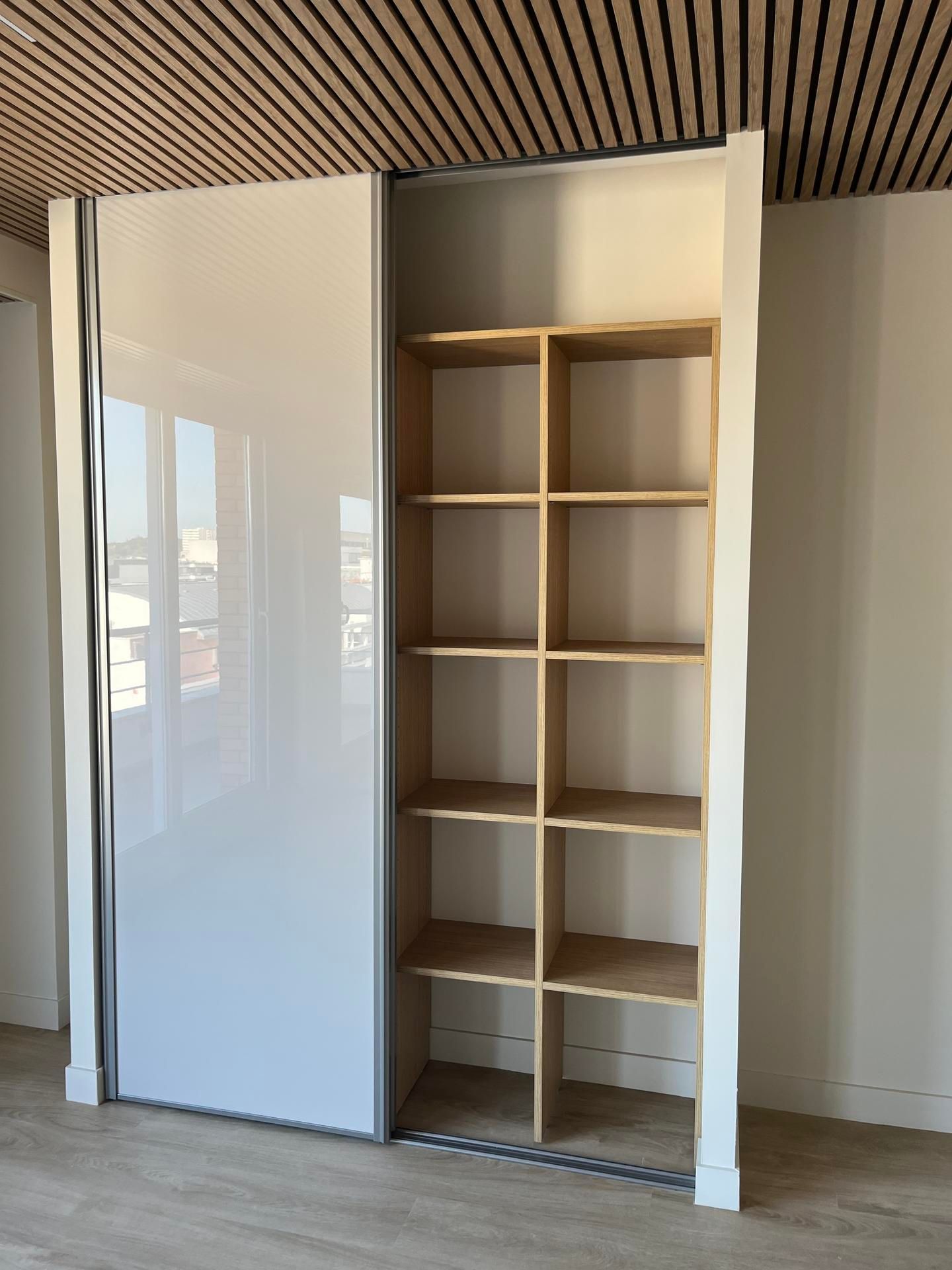 Armoire blanche à portes coulissantes avec étagères ouvertes, étagères en bois clair et plafond en bois clair.