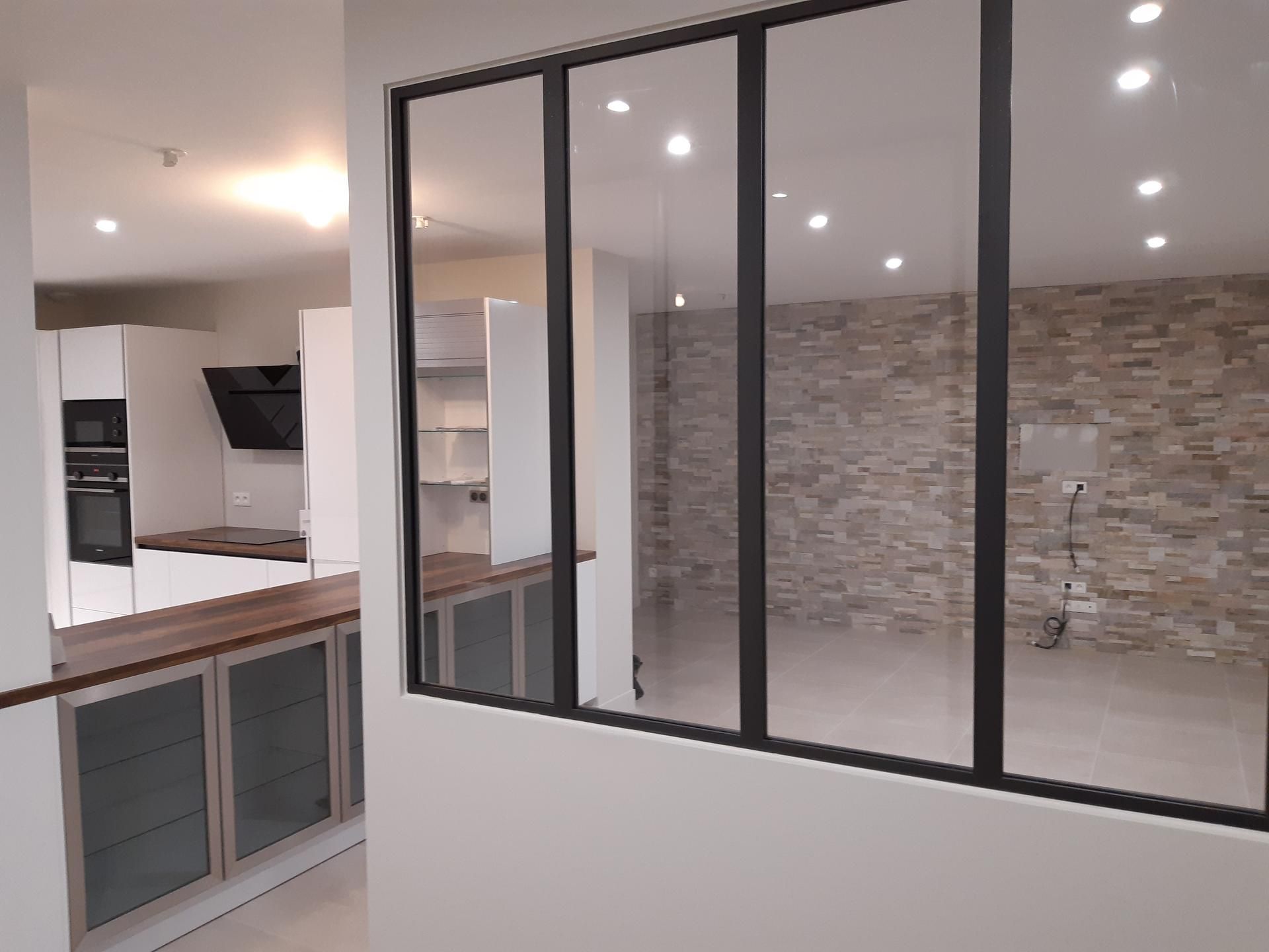 Cuisine et espace de vie modernes avec verrière à cadre noir, mur de briques, armoires blanches et comptoir en bois.