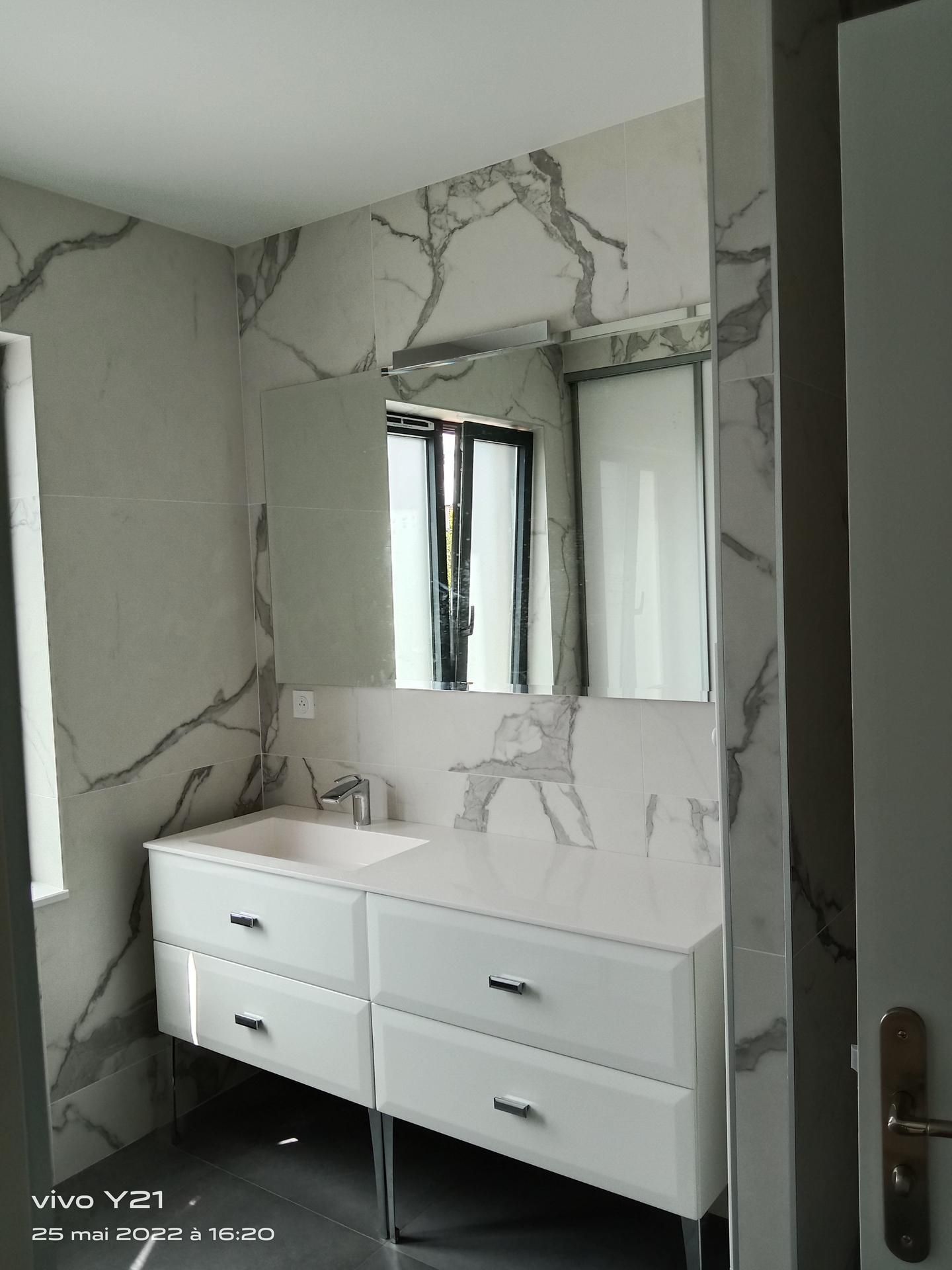 Salle de bain moderne avec vanité blanche, murs à motifs de marbre, miroir et fenêtre.