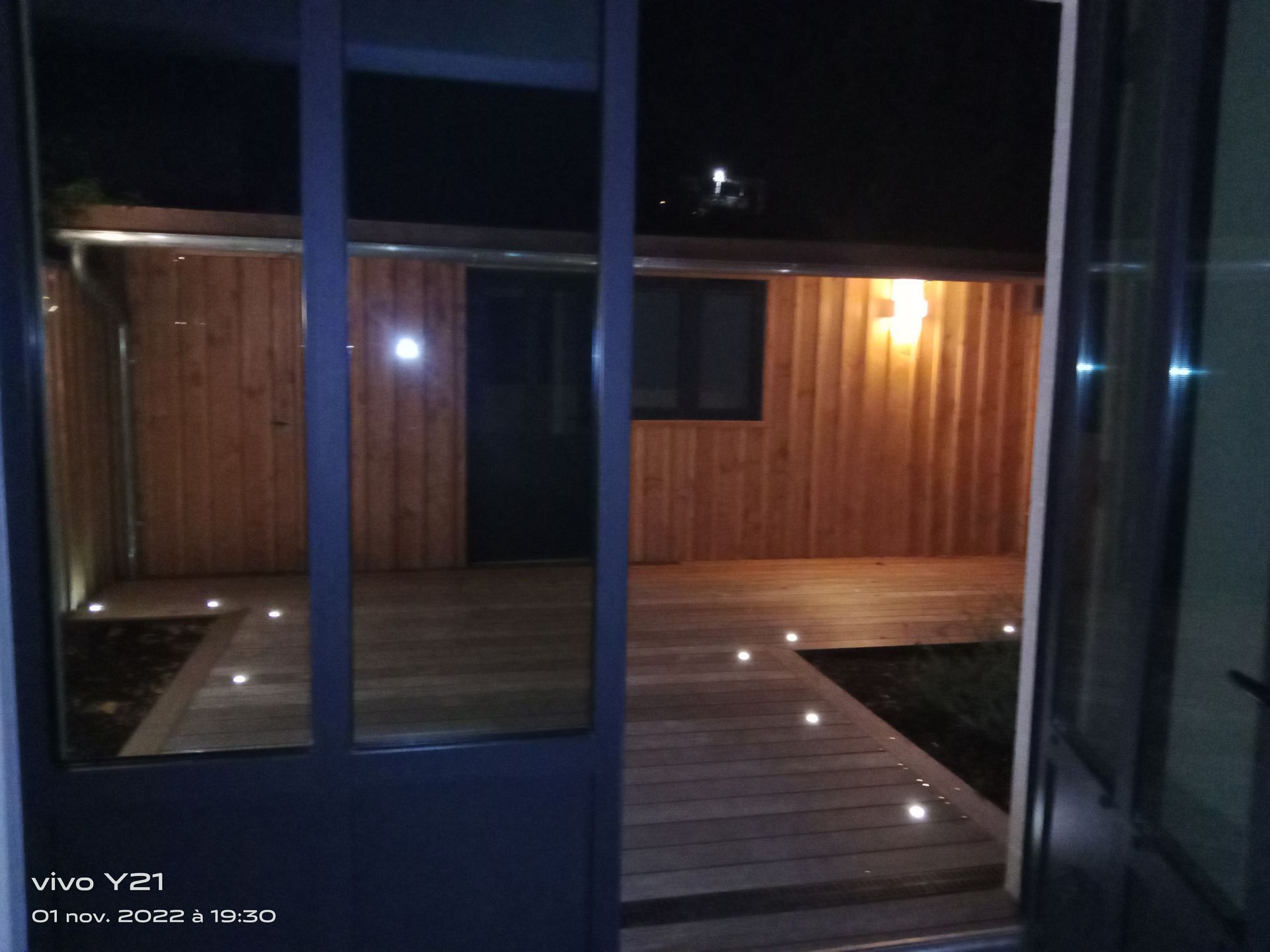 Patio en bois la nuit, éclairé par des spots au sol.