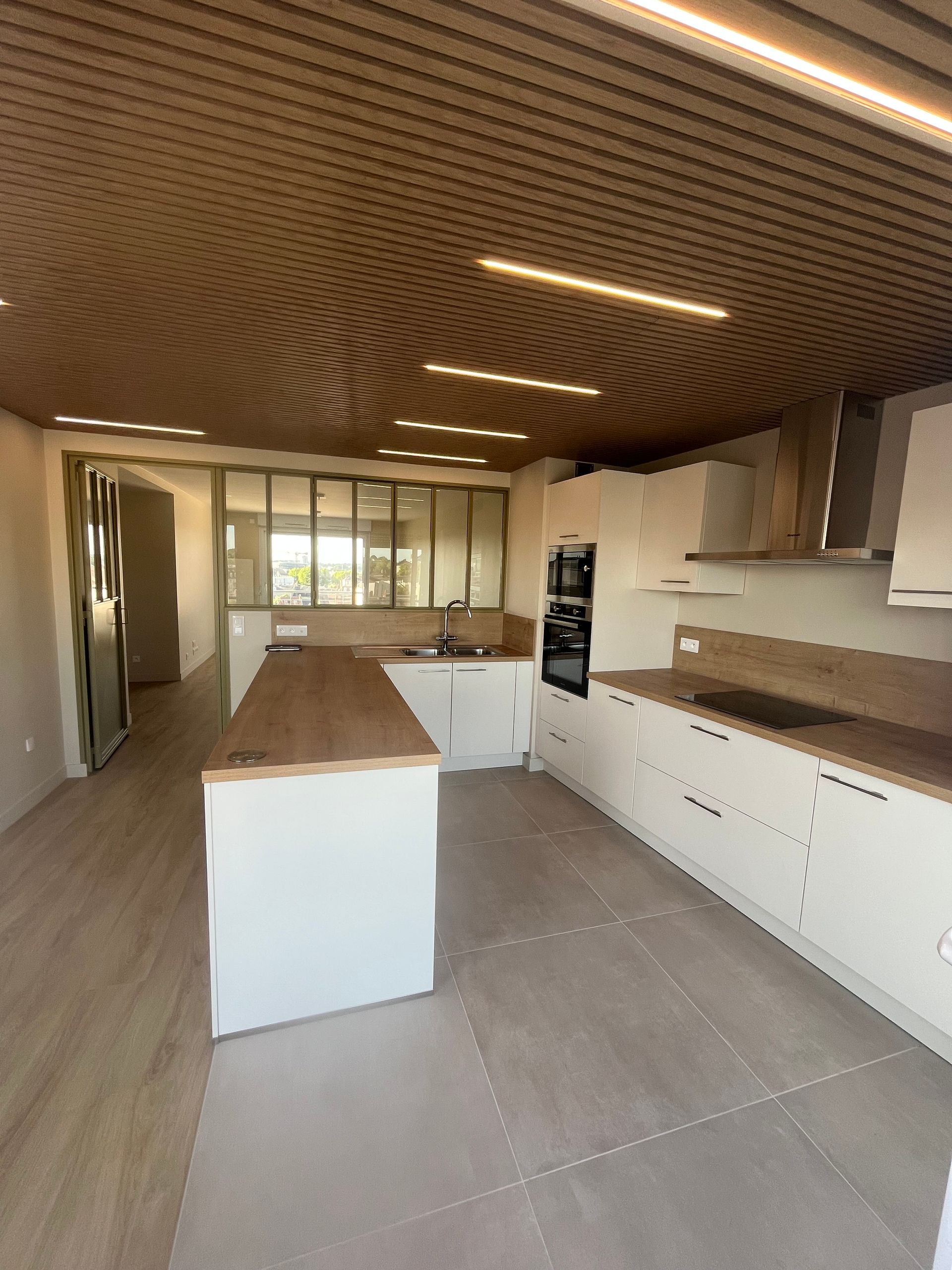 Cuisine moderne avec armoires blanches, comptoirs en bois et plafond en bois à motifs.