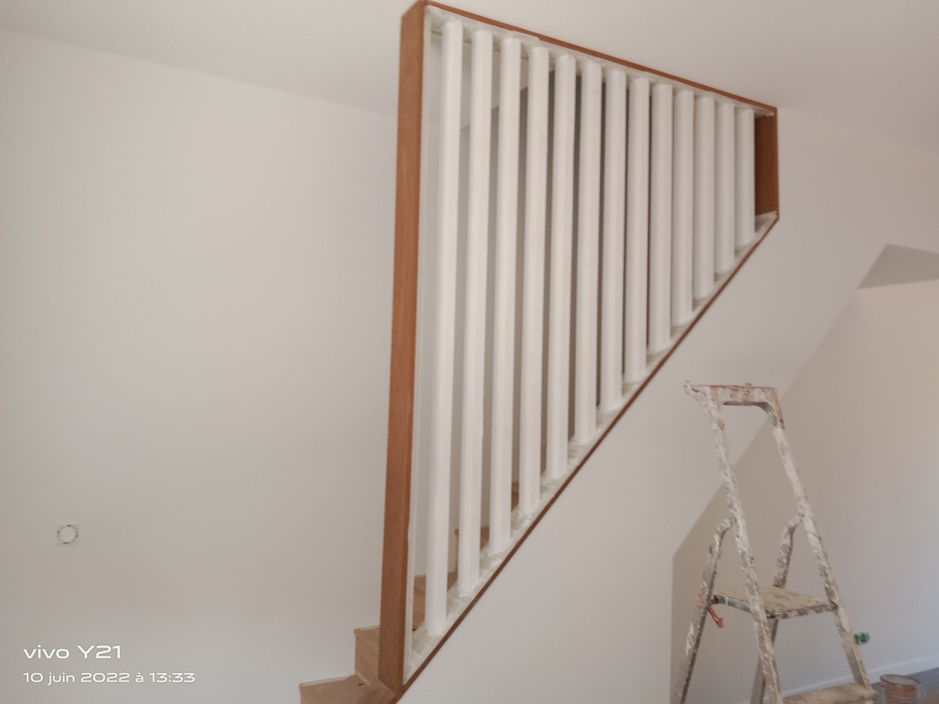 Escalier en bois avec lattes verticales blanches, encadré de bois brun.