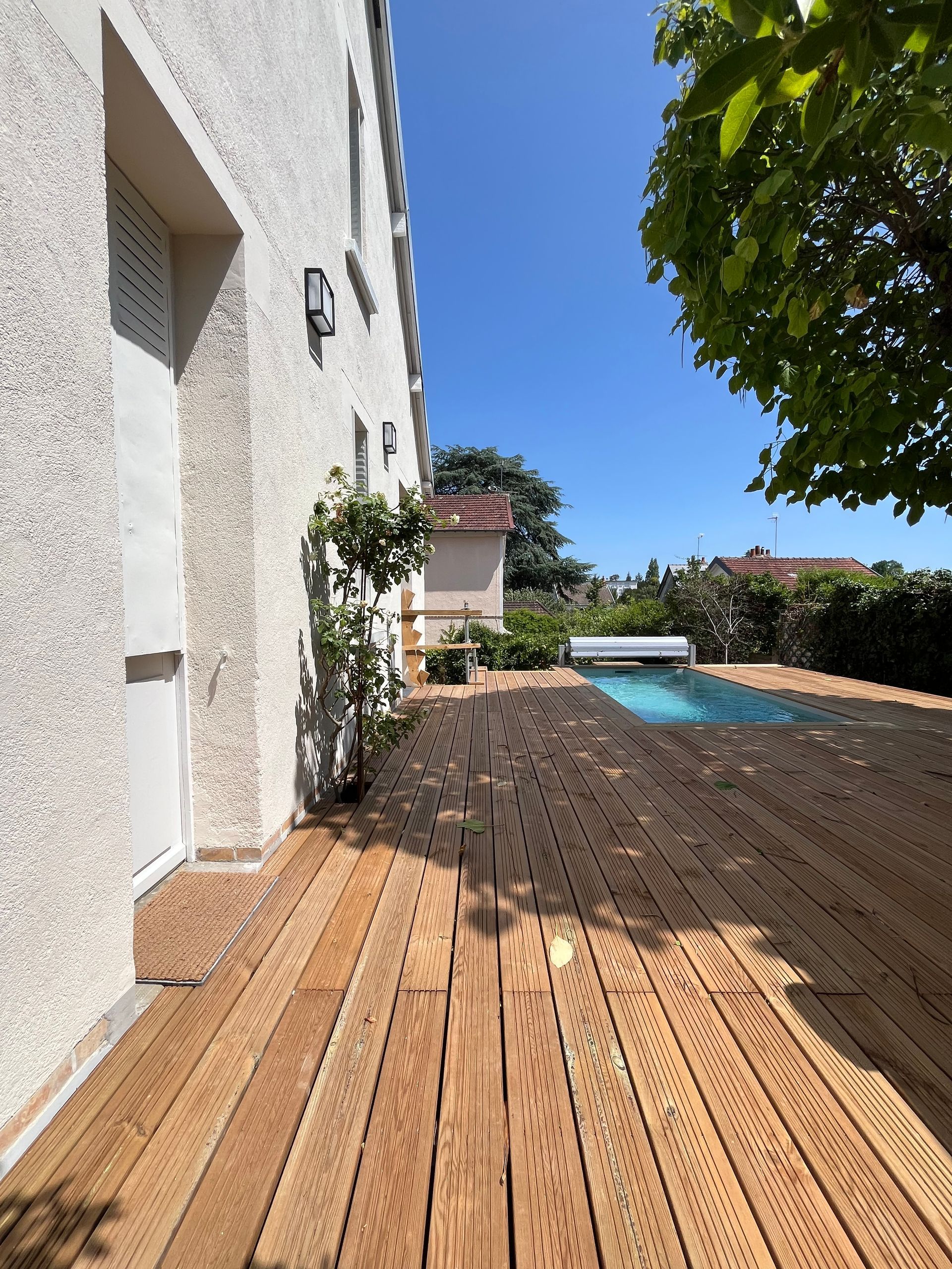 Terrasse en bois près d’une maison blanche et d’une piscine bleue sous un ciel dégagé