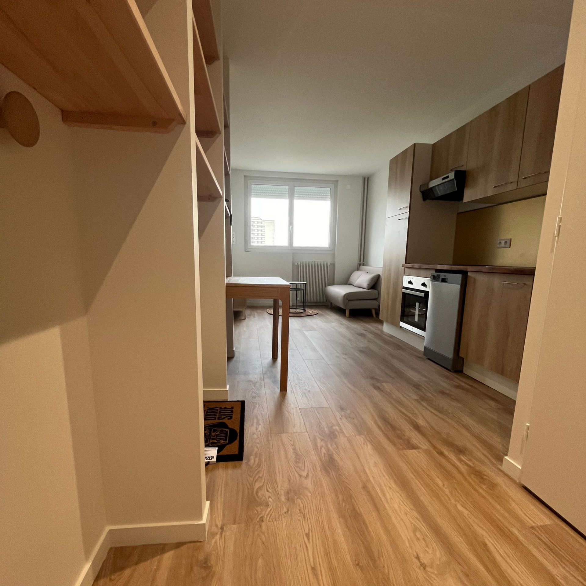 Petit intérieur d'appartement avec parquet, cuisine, salon et fenêtre.