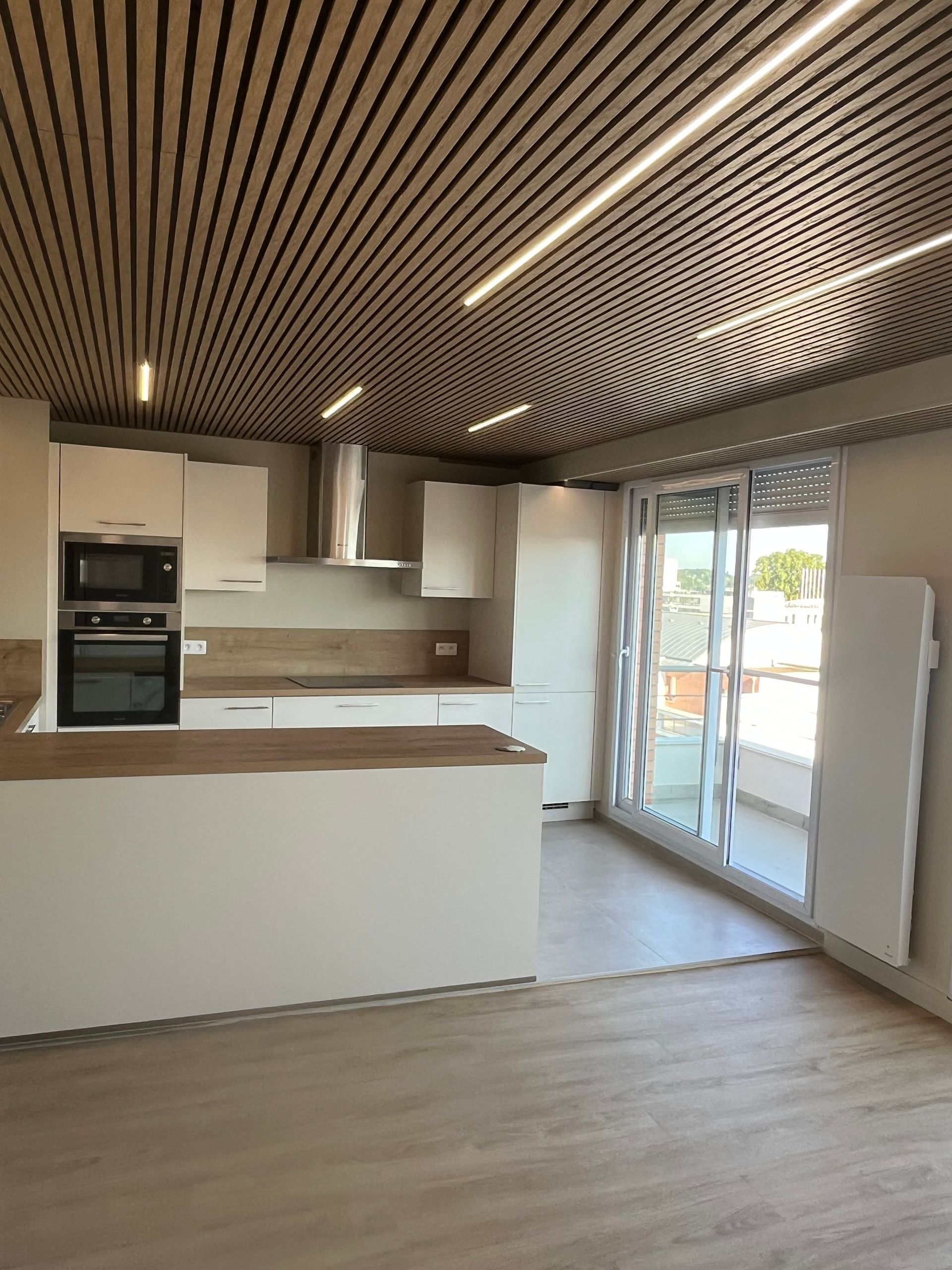 Cuisine moderne avec plafond à lattes de bois, armoires blanches, îlot et portes coulissantes en verre