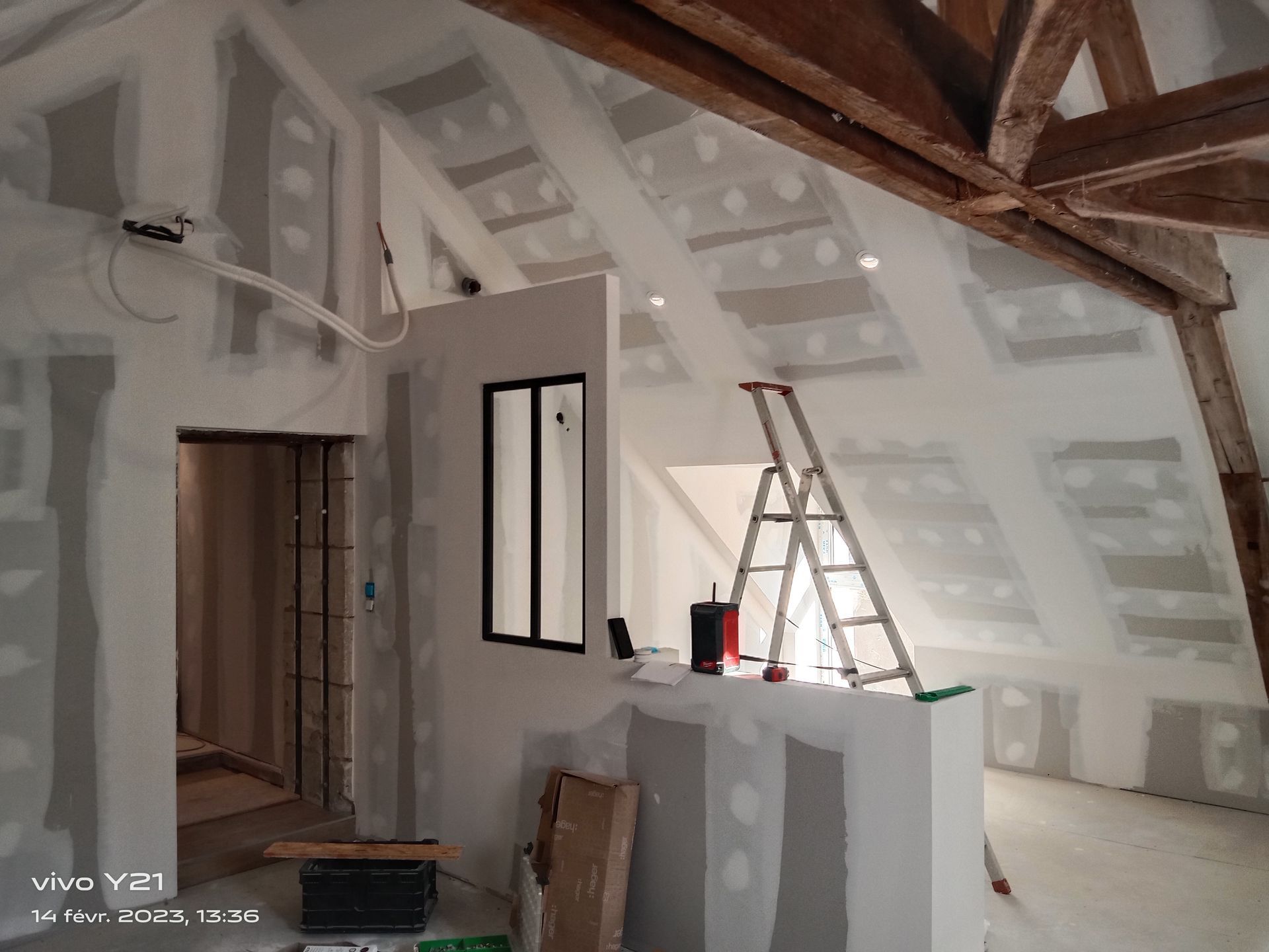 Intérieur d'un grenier non aménagé, avec cloisons sèches et poutres apparentes.