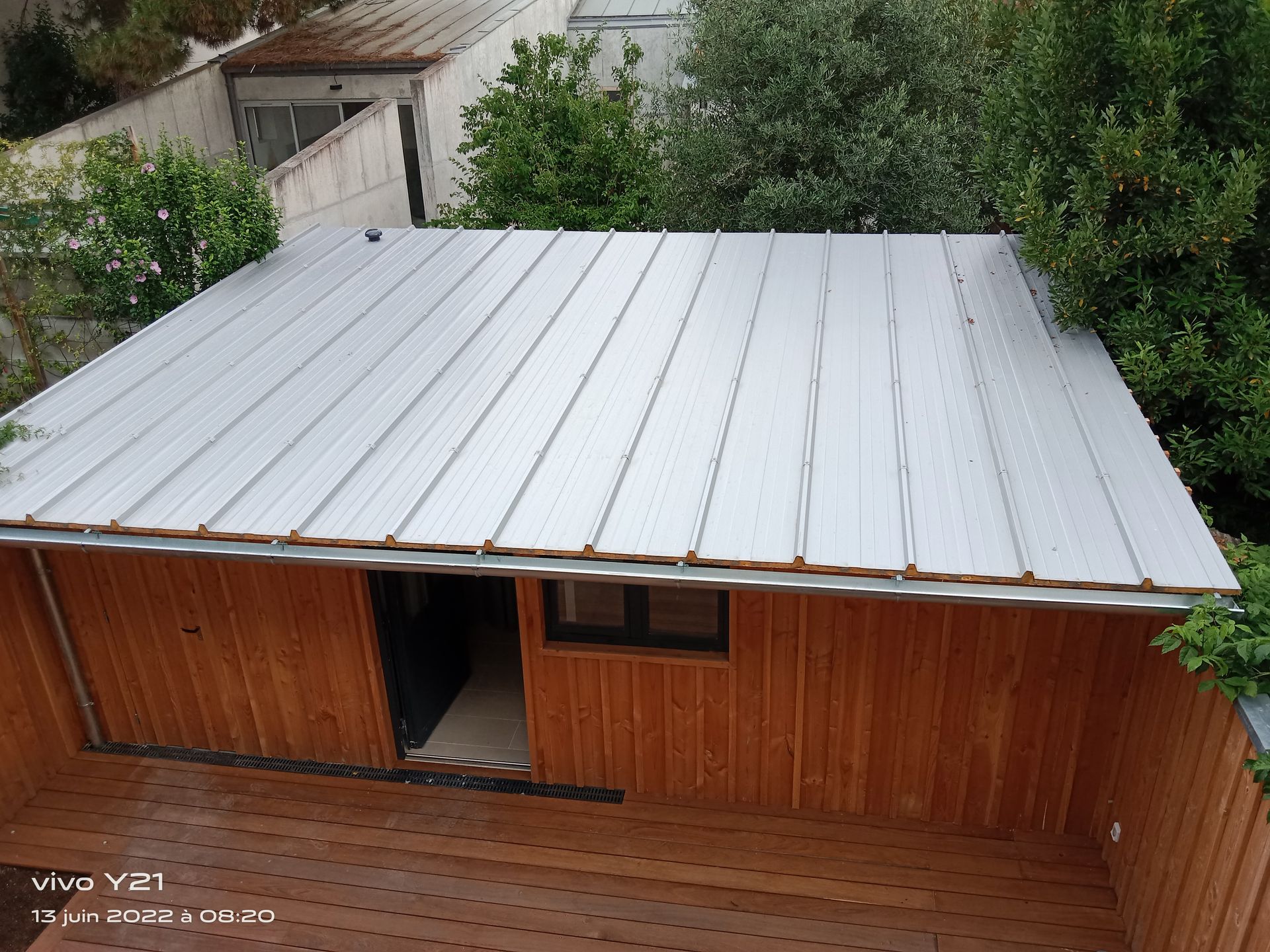 Bâtiment en bois avec toiture en métal entouré de verdure.