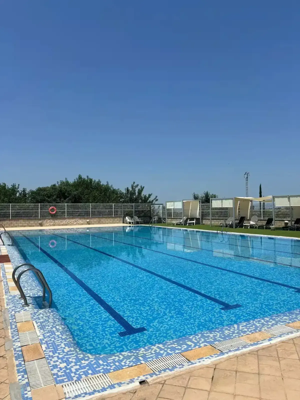 Piscina con agua azul y carriles marcados bajo un cielo azul claro.