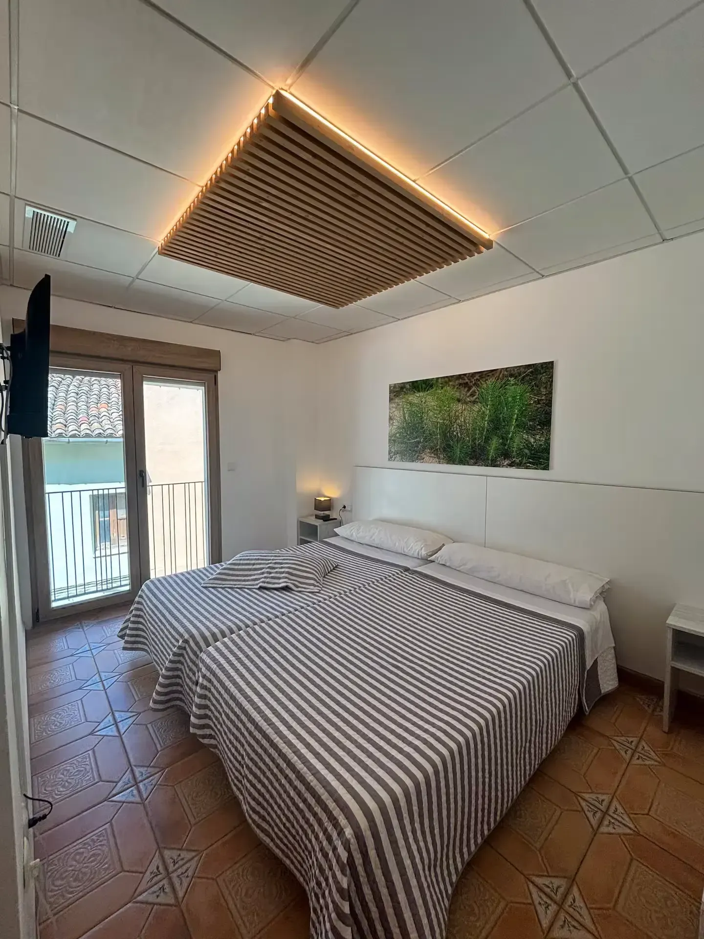 Dormitorio con dos camas, mantas de rayas y un techo de madera con iluminación cálida.