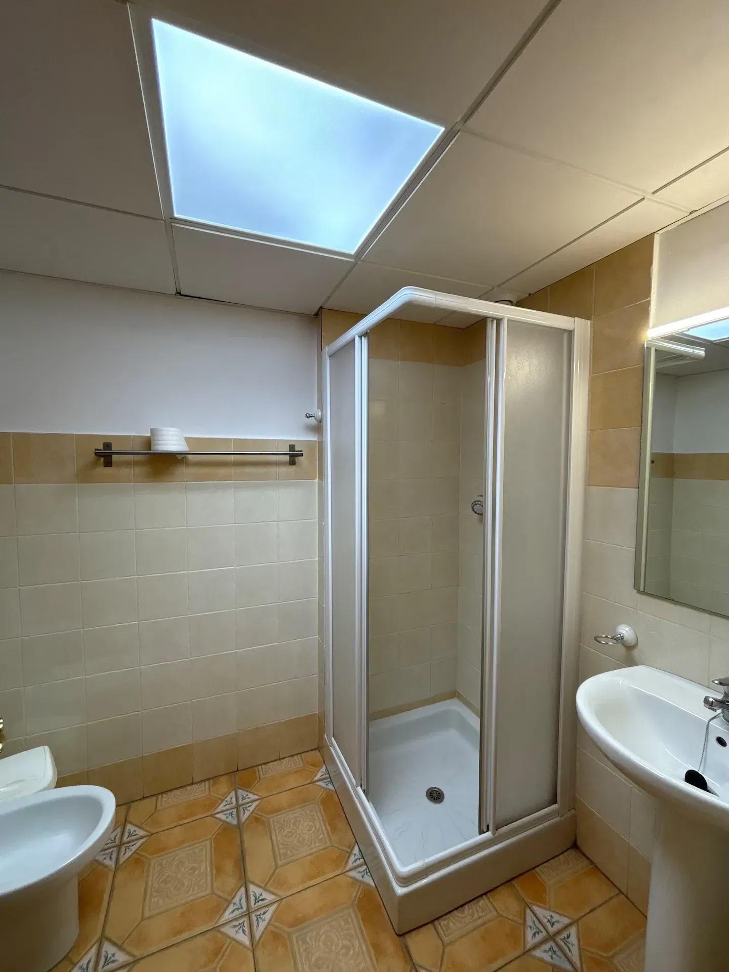 Baño con ducha, lavabo, inodoro y tragaluz; paredes y suelo de baldosas.